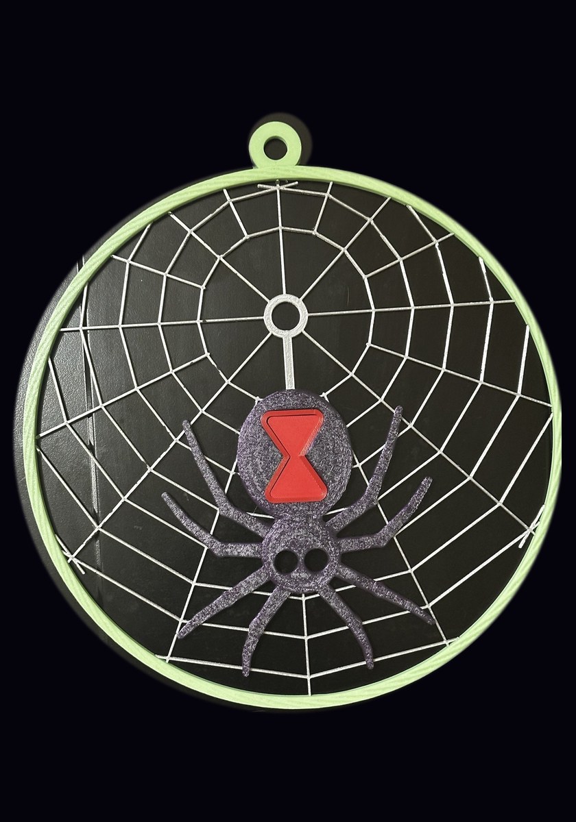 Large glow black widow web in daylight: a pale green ring around a silver web with a black widow spider and a red hourglass